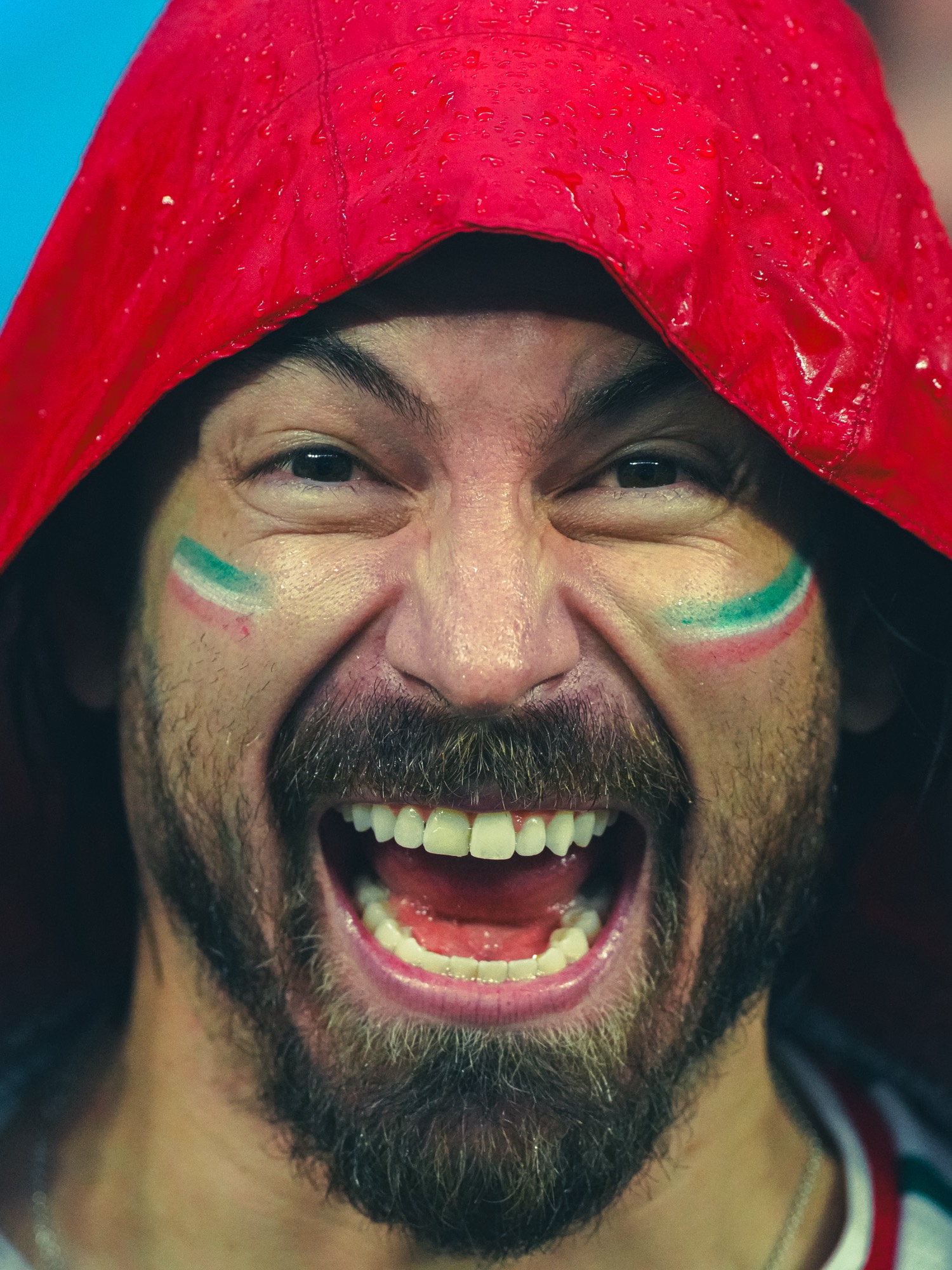 Aficionado con el rostro pintado grita bajo una capucha roja en la lluvia